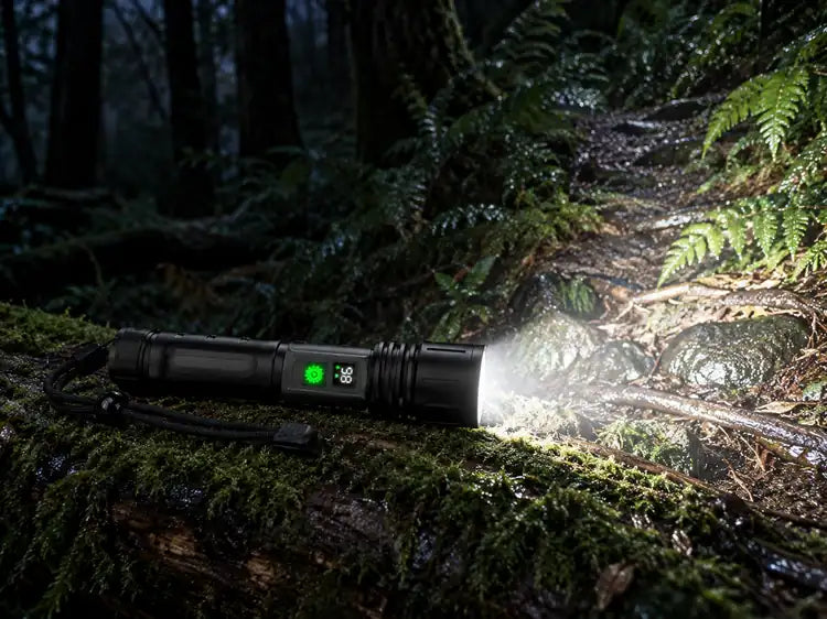 Night-Reach flashlight lying on a mossy log at night, its wide beam lighting ferns and the trail ahead
