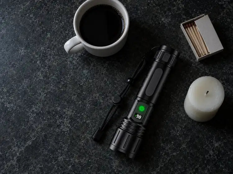 The flashlight on a dark kitchen counter beside a mug, a box of matches and an unlit candle