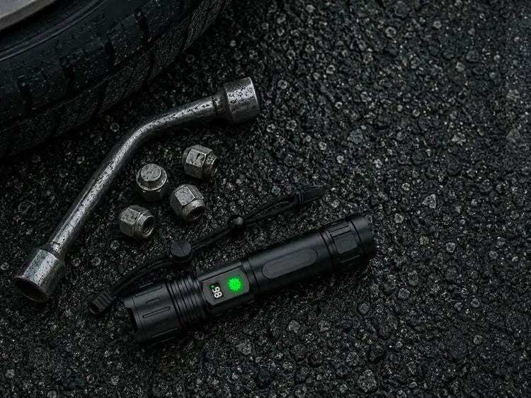 The flashlight on wet asphalt beside a wheel wrench, wheel nuts and a tire